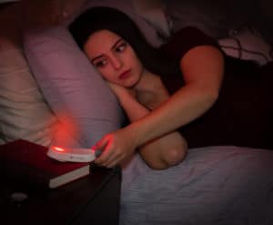 Woman reaching for the TrueLight Luna Red Portable Nightlight + Flashlight on her night stand